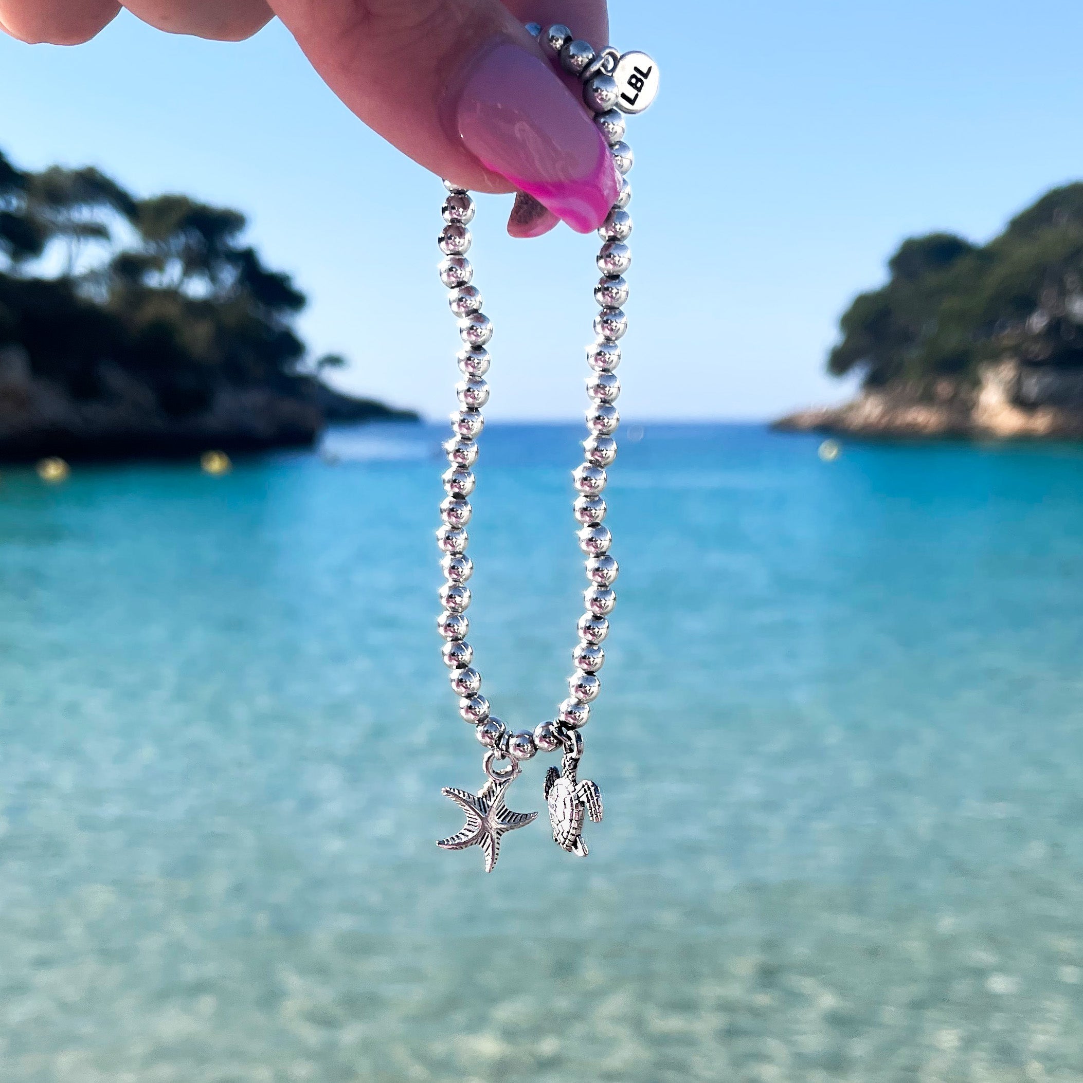 Travel bracelets held in front of the ocean, jewellery trends for 2025