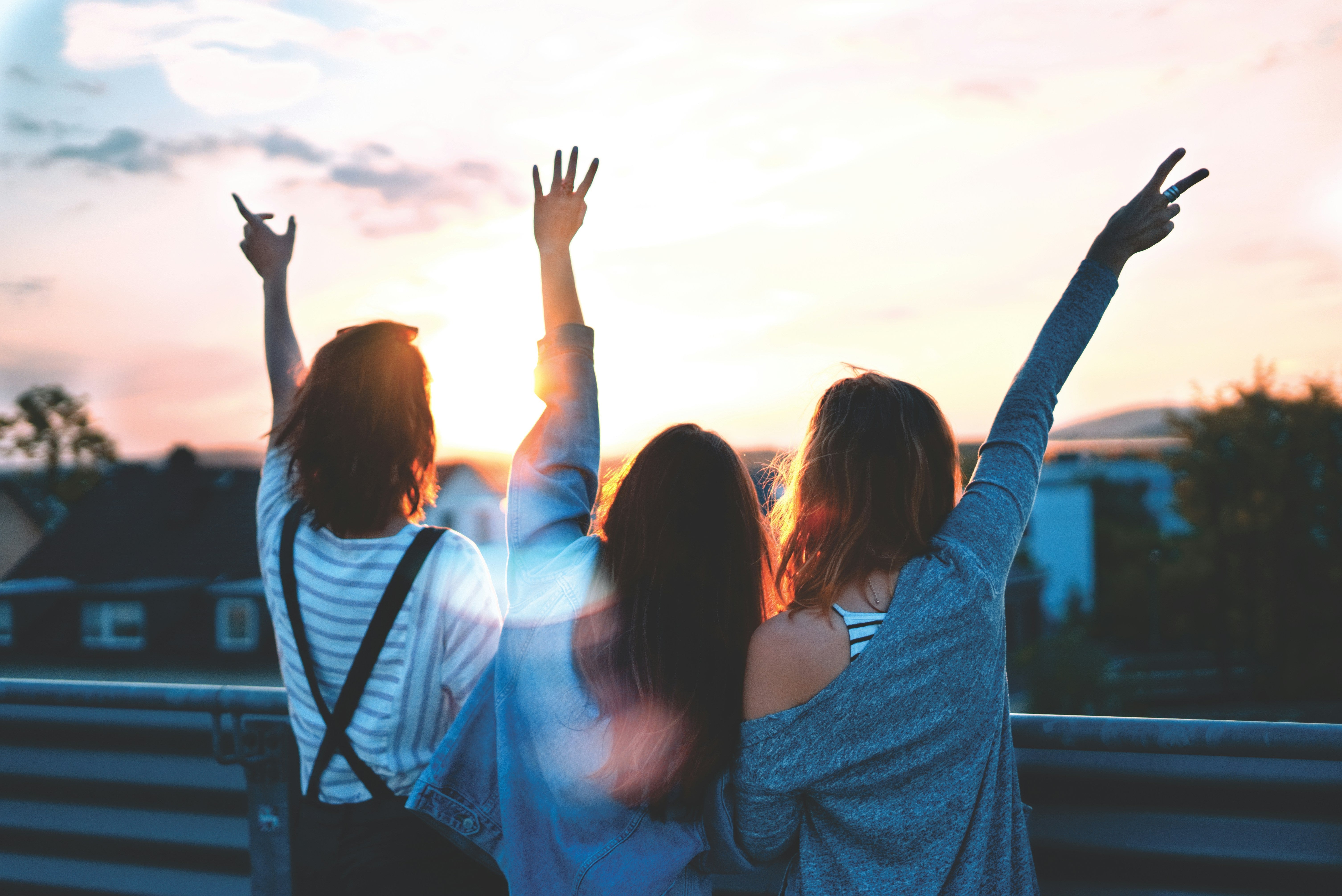 three women with friendship bracelets staring into the sunset with their arms in the air