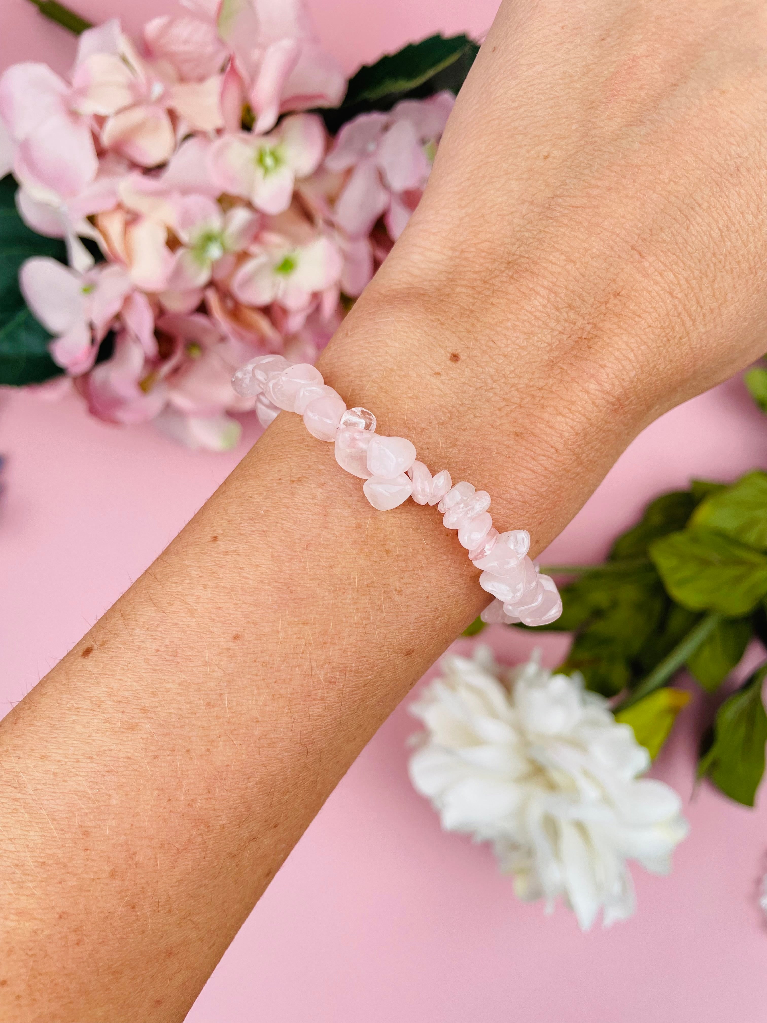 Woman's arm with healing crystal bracelet, the background I pale pink with floral decorations