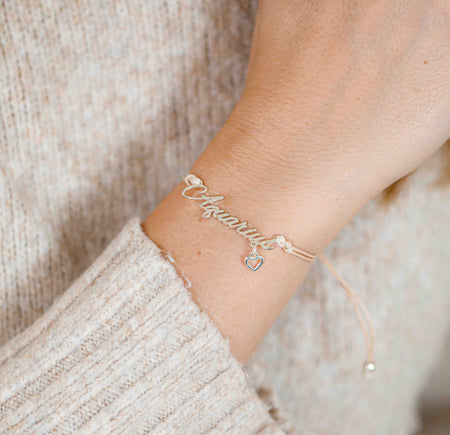 A woman wearing a delicate bracelet with the word “Aquarius” and a tiny heart charm, a meaningful zodiac gift for her.