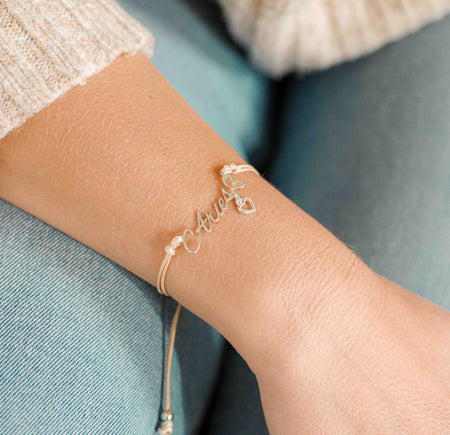A woman wearing a dainty bracelet with the word “Aries” and a small heart charm, a lovely zodiac-inspired gift for her.