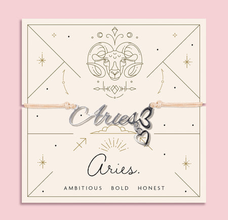 Peach cord bracelet featuring a silver 'Aries' script charm with heart pendant, presented on a zodiac card with ram illustration and personality traits
