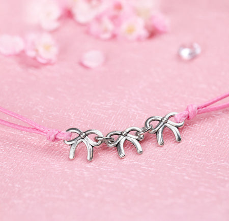 A close-up image of a cute friendship bracelet with pink cord and three small silver-plated bows, creating a perfect gift for a friend