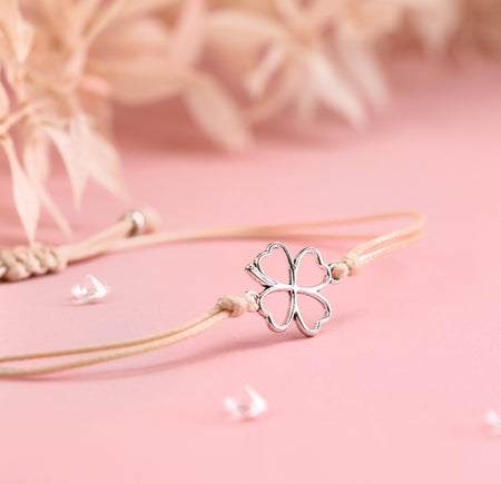 A close-up of a friendship bracelet with beige cord and silver-plated clover bracelet charm. A good luck gift for a friend under £10