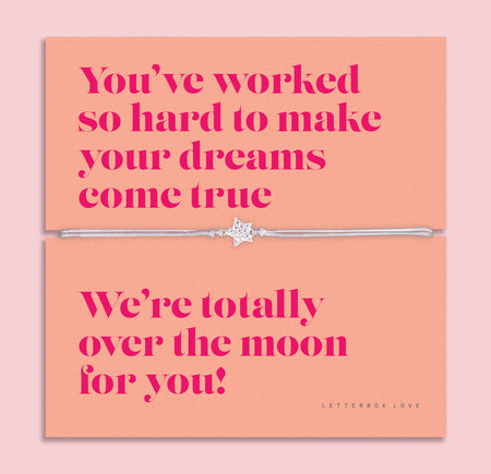 Dreams Come True bracelet with a star charm on a silver band, displayed on a vibrant coral message card with bold pink lettering, celebrating achievement and success