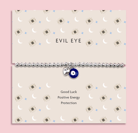 Silver-plated beaded bracelet featuring a deep blue evil eye charm and a small heart charm, displayed on a cream sentiment card with moon and star illustrations and the words “Good Luck, Positive Energy, Protection.