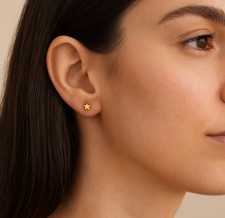 Close-up side profile of a woman wearing delicate gold star stud earrings, approximately 0.5cm in size. The small earrings sit neatly on the earlobe, showcasing their subtle and minimalist design, ideal for everyday wear.