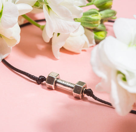 Small dumbbell charm on a friendship bracelet with white flowers around it. A cute gift for a female gym goer