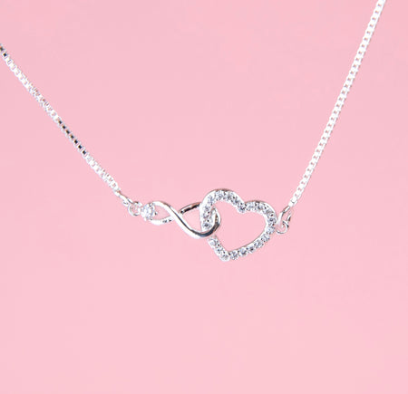 a silver-plated bracelet detail shot of a cubic zirconia hollow heart connecting with an infinity charm on a chain. A cute gift for a daddy and daughter