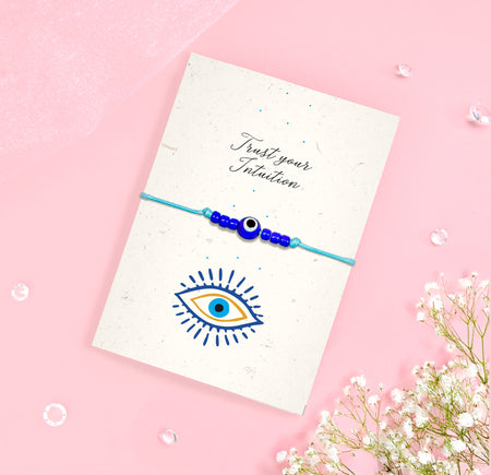 Trust Your Intuition bracelet with Evil Eye charm and blue beads on eco-friendly seeded card with floral design and sentiment 'Trust Your Intuition'.
