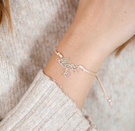 A woman wearing a stylish bracelet with the word “Leo” and a small heart charm, a thoughtful zodiac-inspired gift for her.