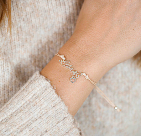 A woman wearing a delicate bracelet with the word “Libra” and a tiny heart charm, a beautiful zodiac bracelet gift for her.
