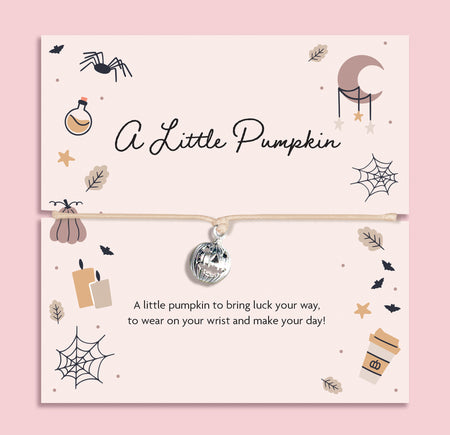 Adjustable beige cord bracelet with silver pumpkin pendant, displayed on blush autumn-themed card with pumpkins, candles, leaves, moon, and spider web illustrations. Perfect Halloween or autumn gift.