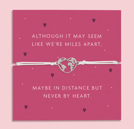 A white adjustable bracelet featuring a heart charm with a world map design, displayed on a deep pink backing card with the message: