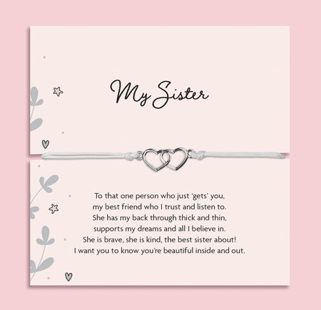 My Sister bracelet featuring two silver interlocking heart charms on an adjustable cord, presented on a blush pink card with a heartfelt message about sisterhood. Wrapped in pink tissue paper, ready for gifting. A sentimental jewellery gift for sisters, perfect for birthdays, Christmas, or just to show appreciation. A meaningful bracelet symbolising love, friendship, and connection between sisters.