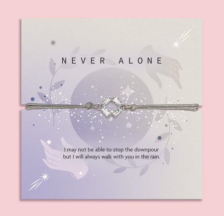 Bracelet with decorative elements on a card with 'Never Alone' text, on a pink background. Cubic Zirconia bracelet to bring comfort to a friend