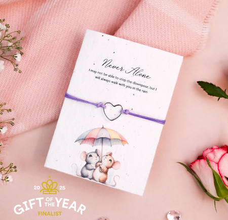 Purple cord bracelet with a silver heart charm, presented on a 'Never Alone' card featuring a sweet illustration of two mice under an umbrella. A comforting gift to remind someone that they are never alone, no matter the challenges they face.