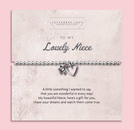 A silver beaded bracelet with a heart and flower charm displayed on a card reading