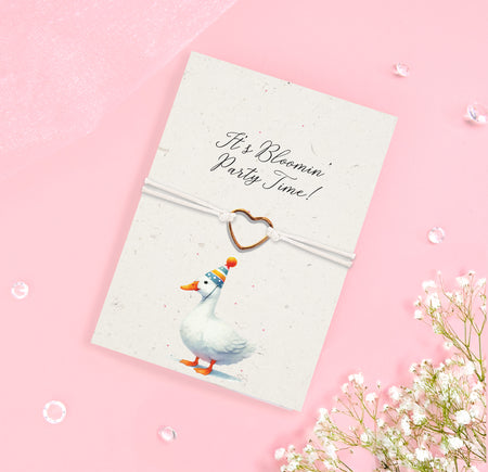 It’s Blooming Party Time bracelet featuring a heart-shaped charm on a white adjustable cord with a whimsical duck wearing a party hat on a seeded card. Fun gift for celebrating special occasions.
