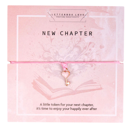A pink bracelet with a small gold key charm, displayed on a pink card with floral designs and the words