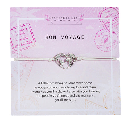 A pink and white card featuring a Bon Voyage message. It has a silver heart-shaped charm in the center, depicting a world map, attached to a white cord bracelet. The card background has various travel-themed stamps, including Melbourne and Venezia. Below the bracelet, a heartfelt message reads: 'A little something to remember home, as you go on your way to explore and roam. Memories you'll make will stay with you forever, the people you'll meet and the moments you'll treasure.'