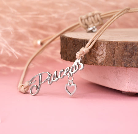 Silver 'Pisces' charm with a heart on a beige cord against a pink background. Jewellery under £20 for her. Pisces bracelet for a friend