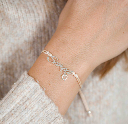 A woman wearing a dainty bracelet with the word “Scorpio” and a small heart charm, a thoughtful zodiac-inspired gift idea.