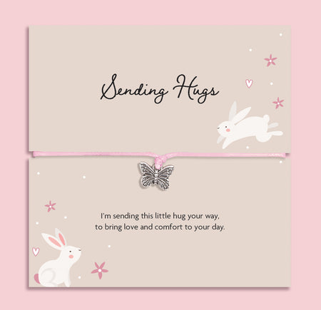 Pink string bracelet with a silver butterfly charm, displayed on a cream card with bunny illustrations and the message “Sending Hugs – I’m sending this little hug your way, to bring love and comfort to your day.