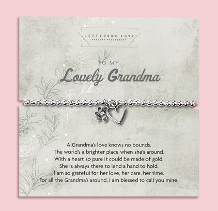 A silver beaded bracelet with a heart and flower charm displayed on a card reading