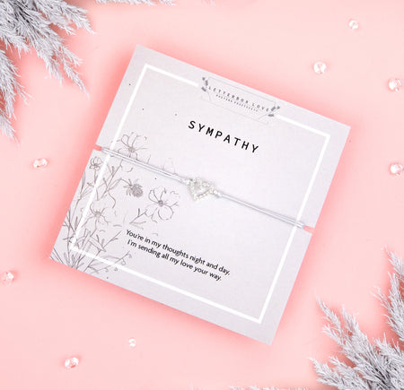 Sympathy bracelet featuring a heart-shaped crystal charm on a white cord, with a heartfelt message on the card reading,