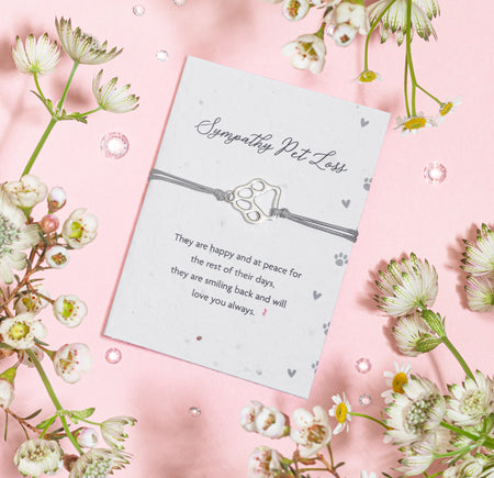 A sympathy seed paper card for pet loss, featuring a paw print charm on a gray bracelet with the inscription