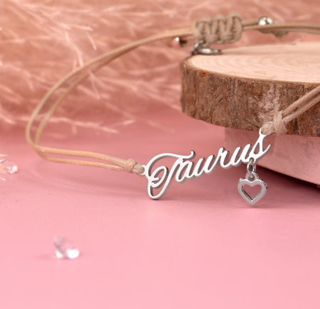 Detail of a silver 'Taurus' bracelet with a heart charm on a pink background. Zodiac bracelet for a friend.