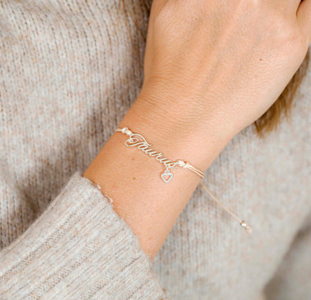 A woman wearing a delicate bracelet with the word “Taurus” and a small heart charm, a thoughtful zodiac bracelet gift for her.