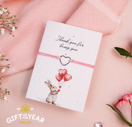 Pink cord bracelet with a silver heart charm, presented on a 'Thank you for being you' card featuring an illustration of a bunny holding heart-shaped balloons. A sweet and thoughtful gift for expressing gratitude and love.