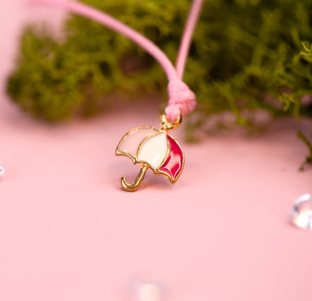 gold umbrella charm with pink accents on a pink string with moss in the background