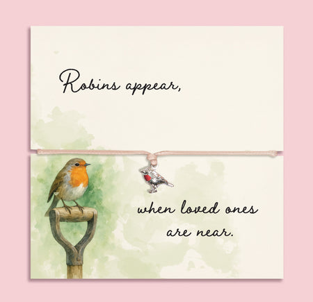 Memorial bracelet with silver robin charm and pink cord, displayed on a sentimental card reading “Robins appear, when loved ones are near,” with soft green watercolour and robin illustration.