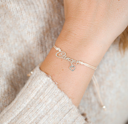 Silver bracelet with 'Cancer' star sign on a wrist against a neutral background. Zodiac jewellery for her.