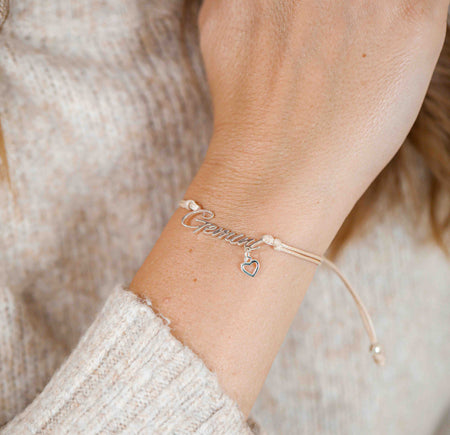 A woman wearing a delicate bracelet with the word “Gemini” and a small heart charm, making a thoughtful zodiac-themed gift.