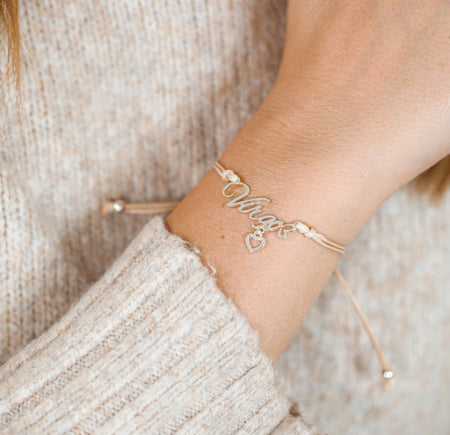 Gold bracelet with heart and Virgo charm on a woman's wrist against a neutral background. A starsign gift for her.