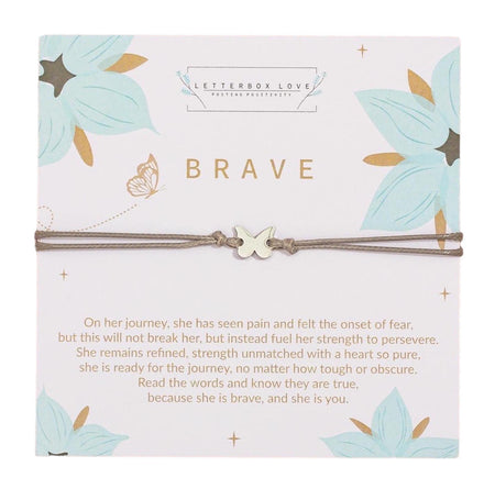 An inspirational 'Brave' bracelet card featuring a minimalist brown cord bracelet with a silver butterfly charm. The top of the square card has the word 'BRAVE' in bold, gold letters, and it's adorned with pastel teal floral and golden butterfly illustrations. Below the bracelet, there's an empowering poem about strength and bravery. The brand 'LETTERBOX LOVE' is noted at the top for positivity.