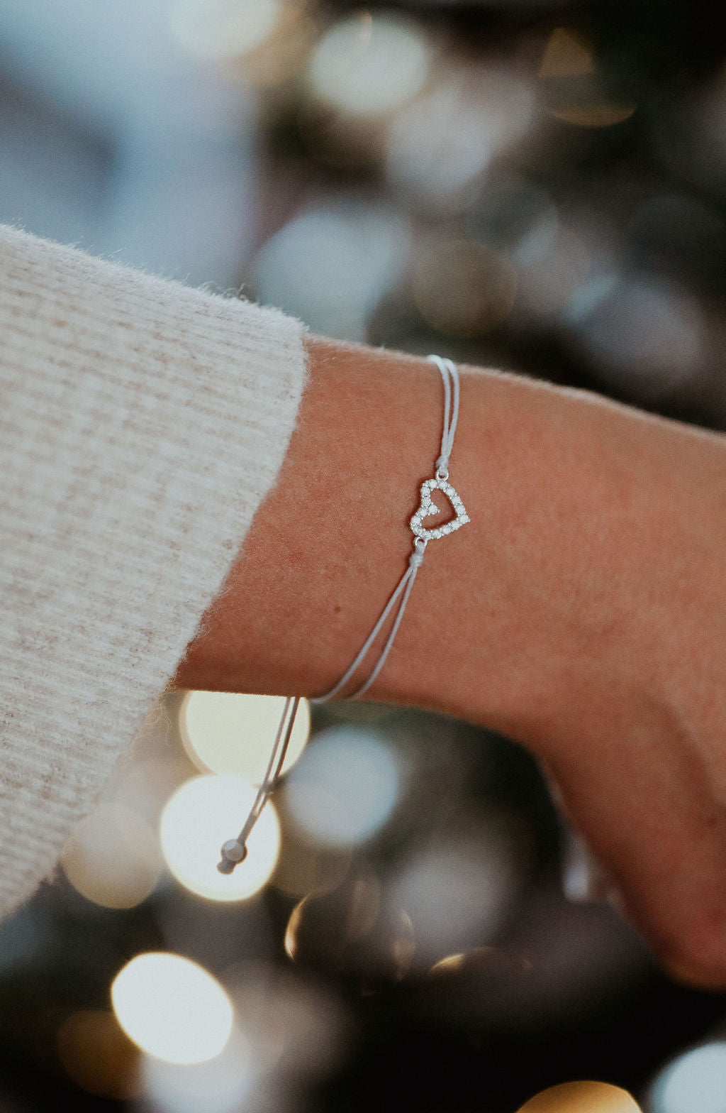 A woman's arm with a small heart bracelet and grey string bracelet