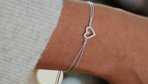 A woman's arm with a small heart bracelet and grey string bracelet