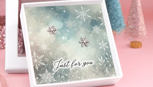 A white gift box with a snowflake pattern card reading "just for you" with two snowflake earrings on