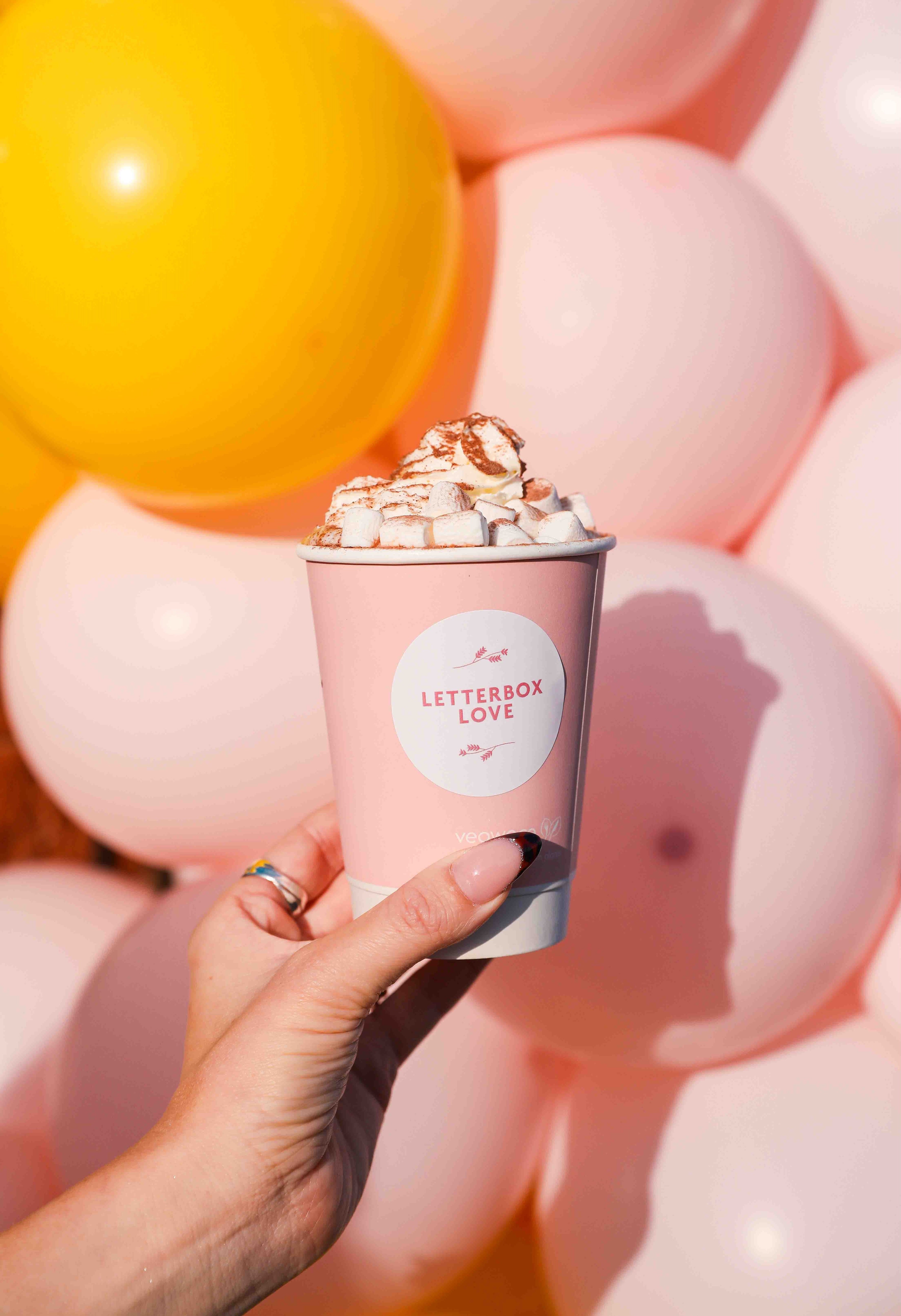 Pink and yellow balloons with a woman's hand and a hot chocolate with whipped cream