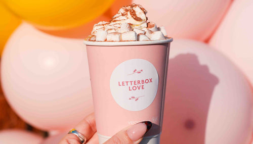 Pink and yellow balloons with a woman's hand and a hot chocolate with whipped cream