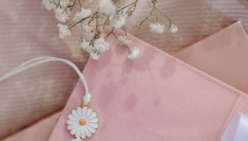 A daisy charm bracelet with white string on a Thank You card with delicate flowers