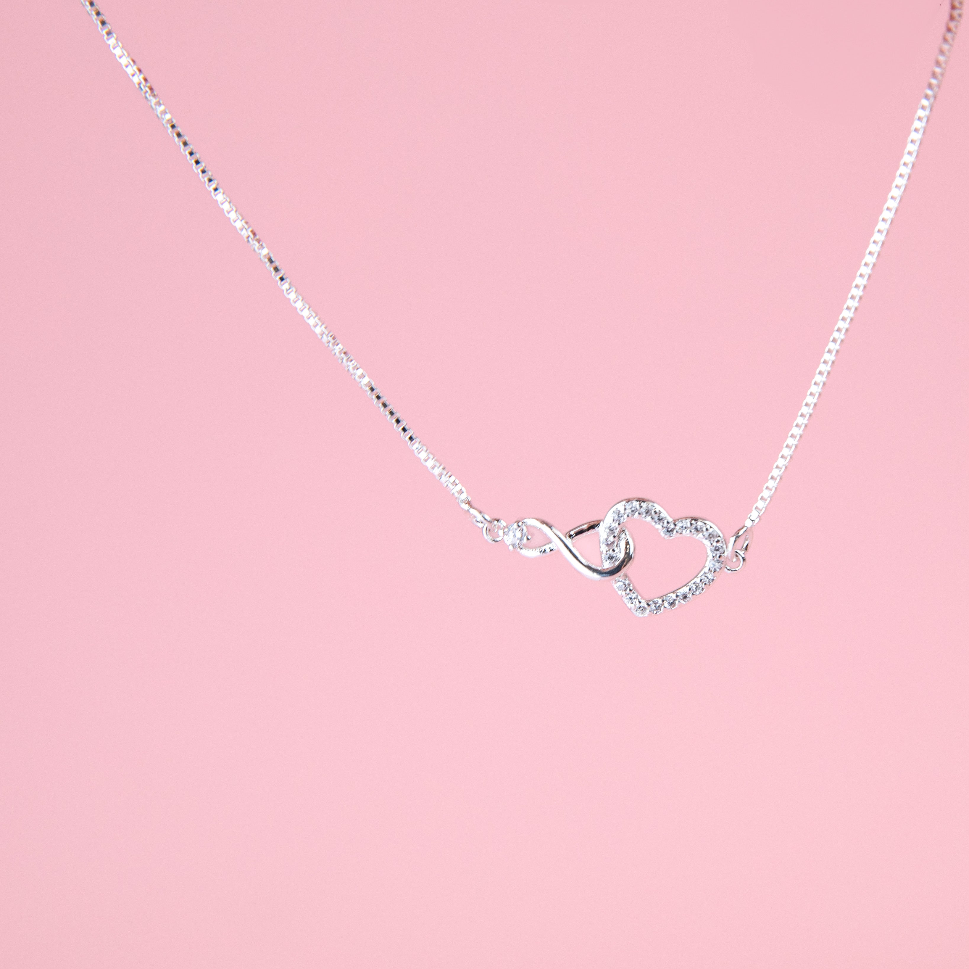 pink background with a silver-plated bracelet with infinity charm interlocked with a heart