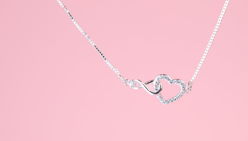 pink background with a silver-plated bracelet with infinity charm interlocked with a heart