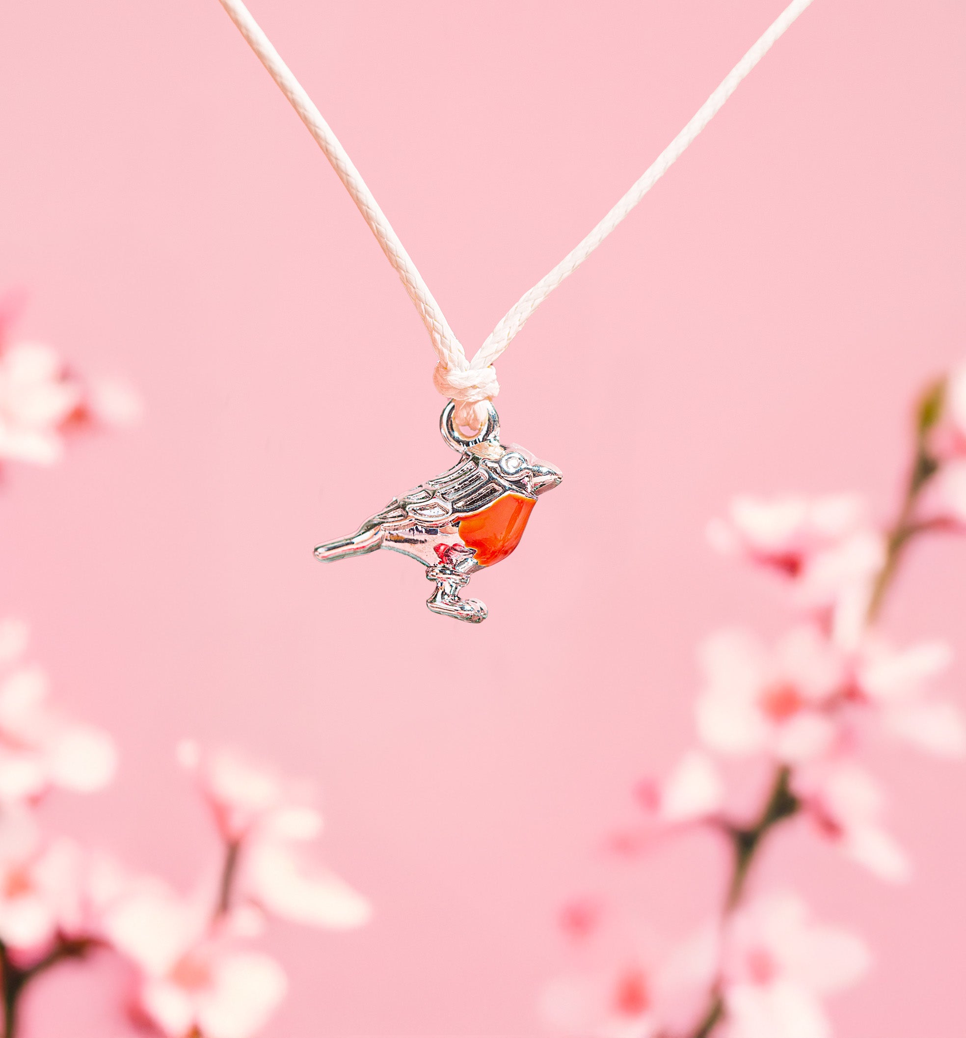 Pink background with a cute robin charm on a bracelet for women. A festive gift under £10 for her.