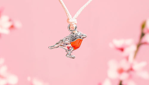 Pink background with a cute robin charm on a bracelet for women. A festive gift under £10 for her.